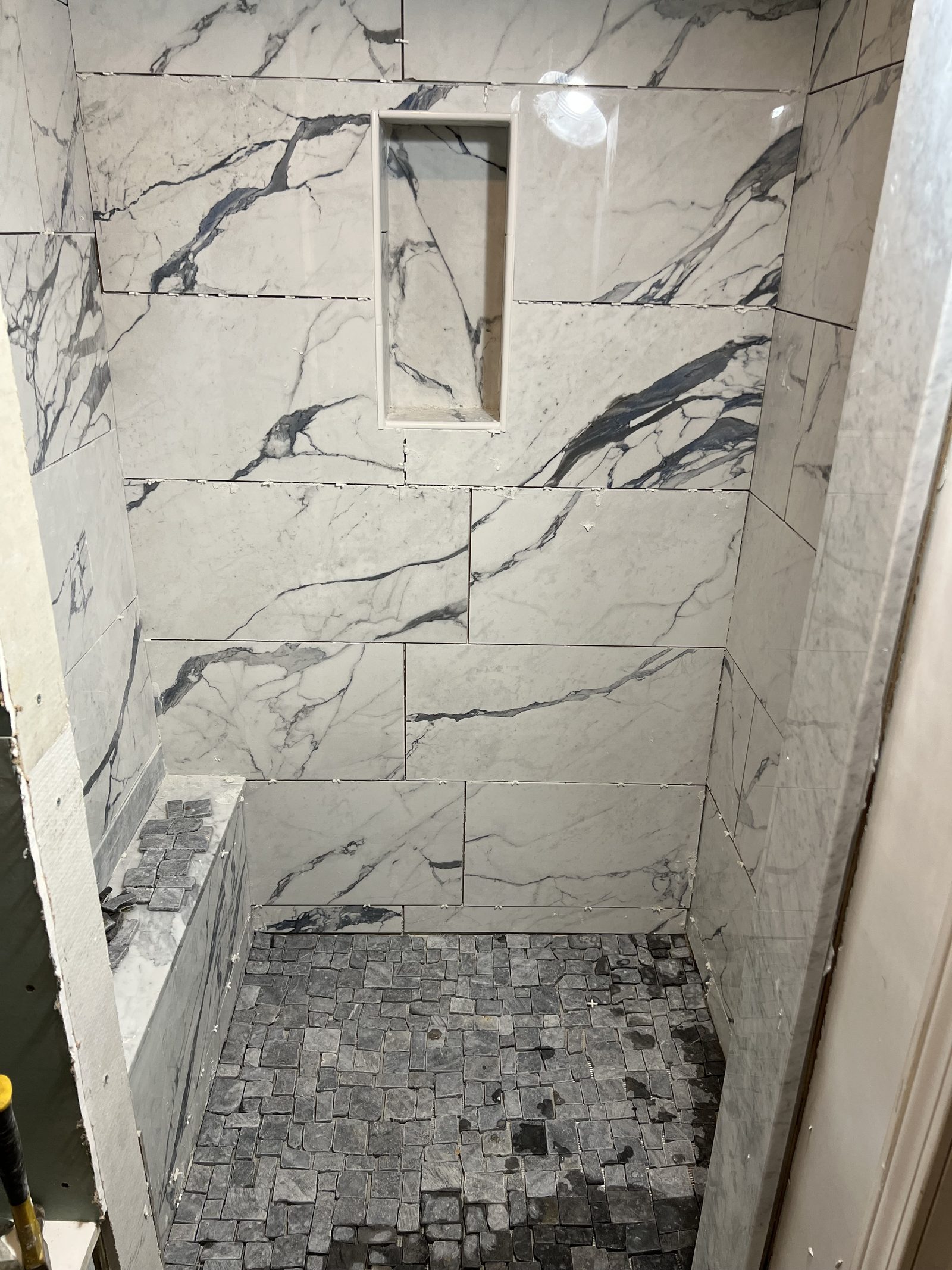 Nearly finished shower with marble-look wall tile, a recessed niche and a mosaic floor